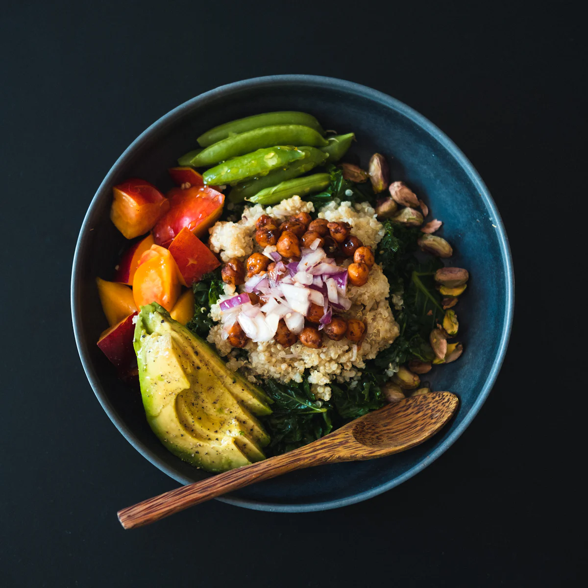 A quinoa bowl with chickpeas, greens, avocado and a wooden spoon