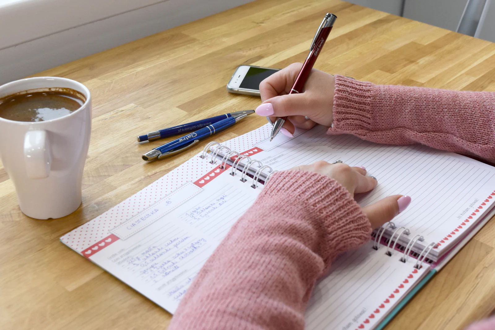 Writing a weekly meal plan in a notebook next to a cup of coffee